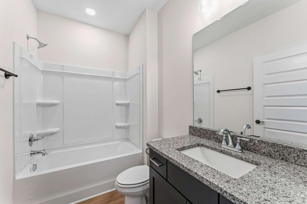 The full bathroom offers a shower-tub combination, granite countertop and navy cabinets.