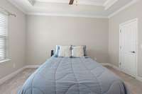 Primary suite alternate view with extra molding in the tall ceilings, ceiling fan, and ample space