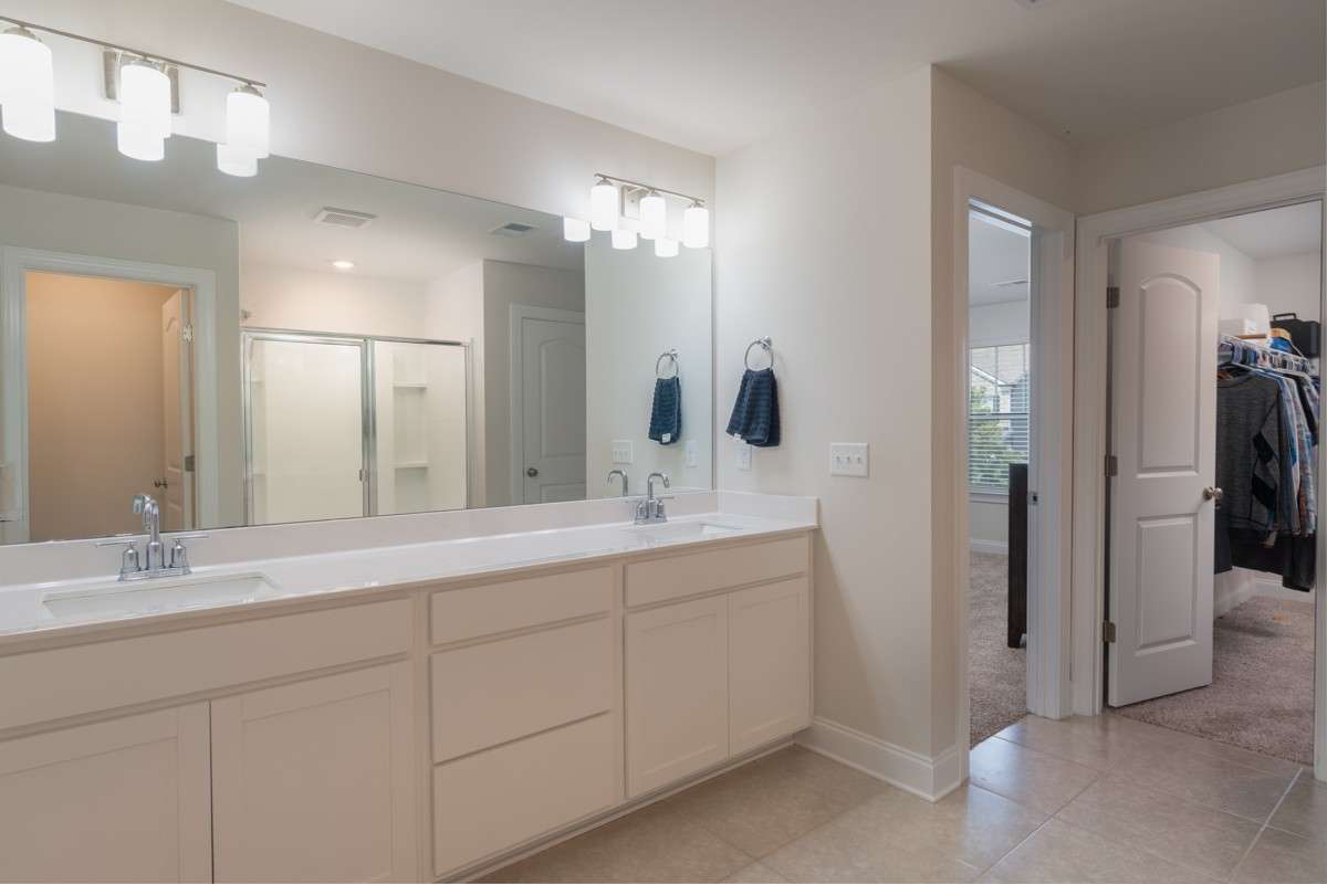 The primary bathroom offers a spacious double vanity, large mirror with modern lighting, and a walk-in shower. Conveniently connected to the primary suite and walk-in closet, it creates a seamless and private retreat