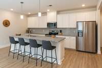 Beautiful kitchen with a Large island. Featuring white cabinetry, granite counter tops, stainless steel appliances and a stylish subway tile backsplash. The virtual staged bar stools give you an idea of just how much space this kitchen has to offer.