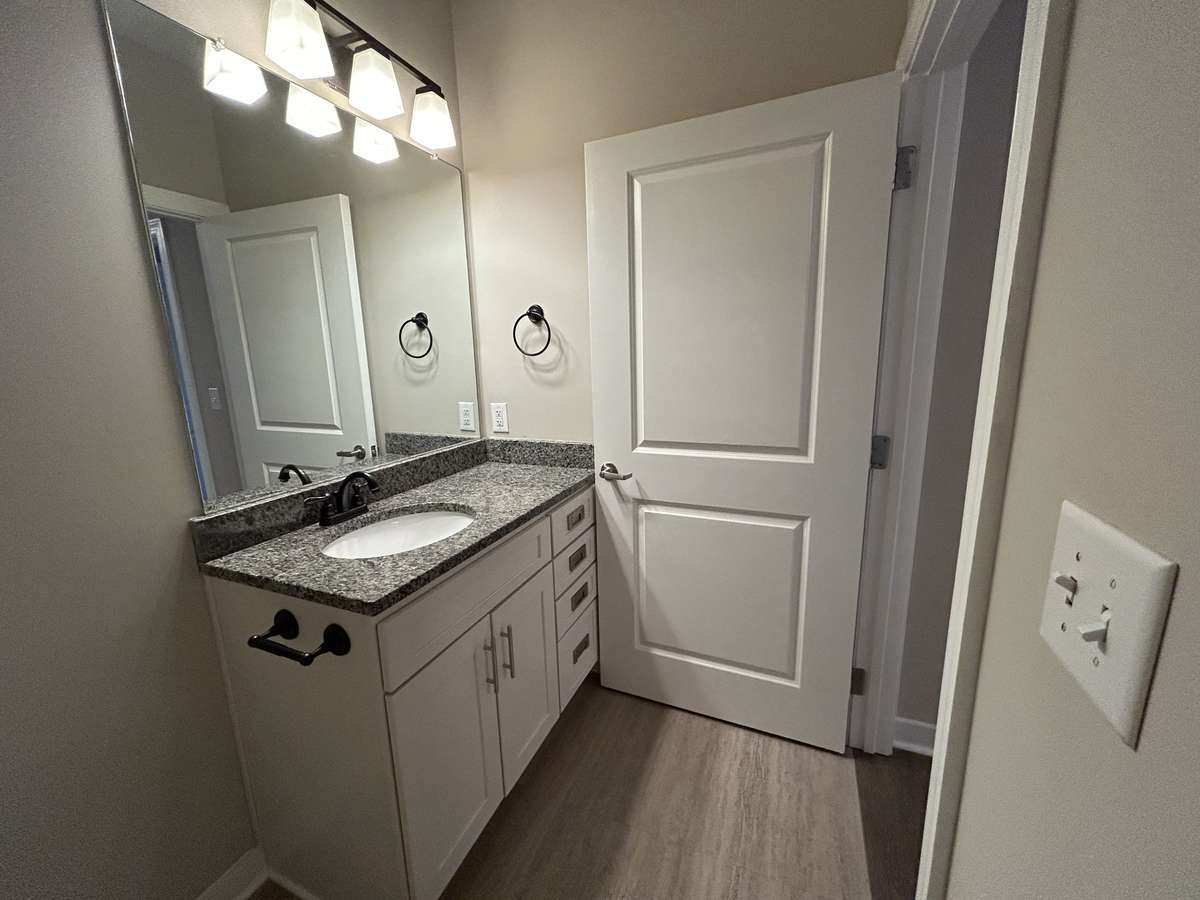 Just outside the bedroom door, a very weldedigned bathroom with a vanity with recessed sink, four drawers and a large space for toiletries under the sink. Ample towel racks, and large mirror with three light fixture above