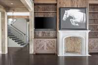The family room features floor to ceiling windows, bookshelves featuring Pecky Cypress, custom beams, and a wood-burning fireplace.