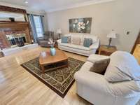 The expansive living room showcases wide-plank flooring, a sophisticated raised tray ceiling, and a striking fireplace that anchors the space with style and comfort.