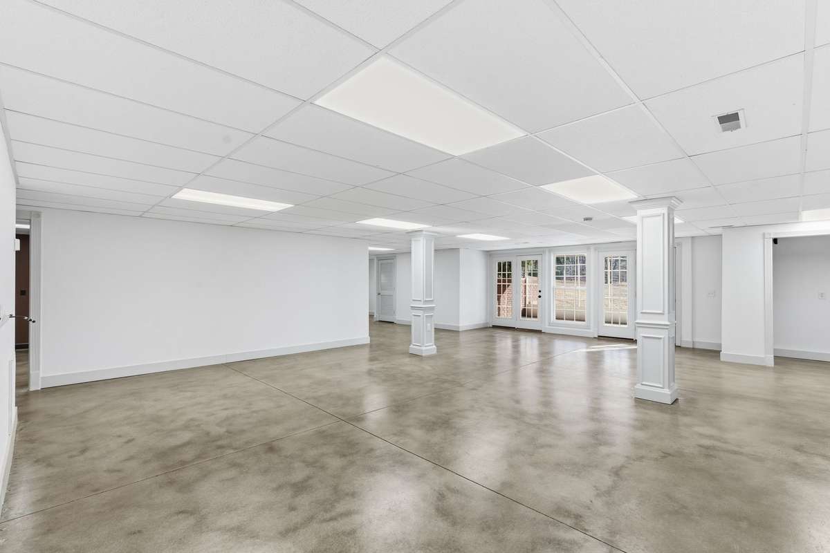 Expansive open area in the finished basement with polished concrete floors, neutral palette, and double doors to the backyard, offering a versatile space for a game room, gym, or large gatherings.