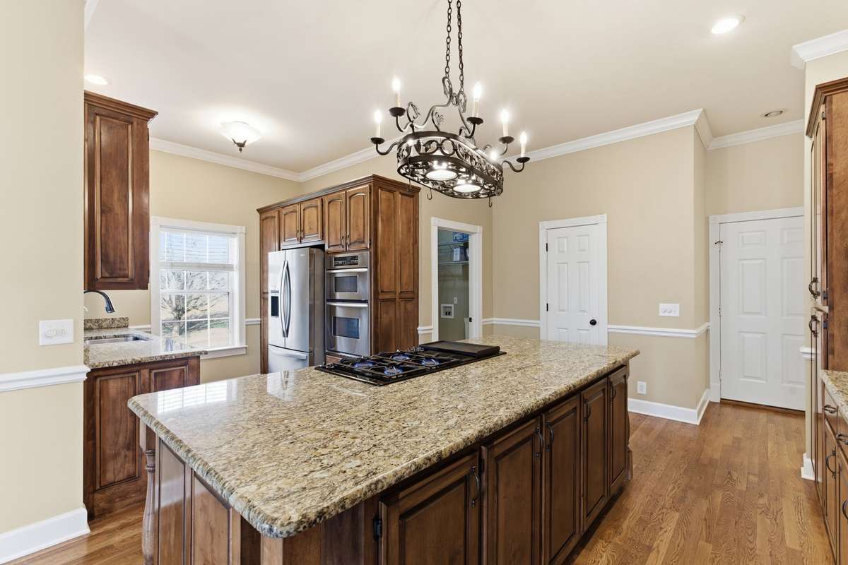 Upscale kitchen showcasing a large granite-topped island with Jenn‑Air cooktop, rich custom cabinetry, built‑in wine storage, and generous counter space, all opening to a cozy breakfast nook perfect for casual dining.
