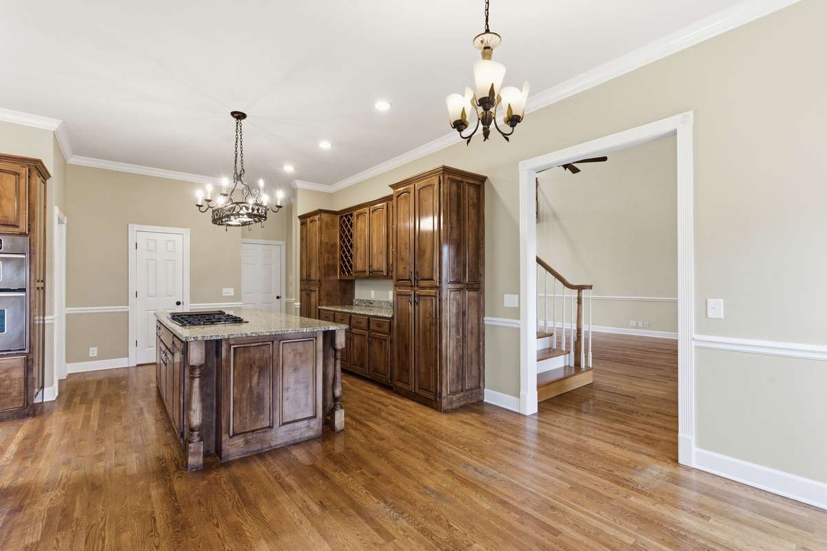 Upscale kitchen showcasing a large granite-topped island with Jenn‑Air cooktop, rich custom cabinetry, built‑in wine storage, and generous counter space, all opening to a cozy breakfast nook perfect for casual dining.