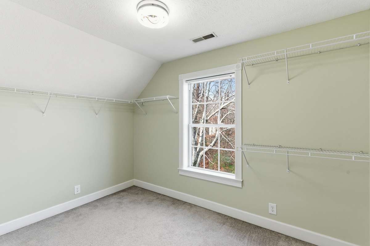 Spacious upstairs secondary primary bedroom featuring two ceiling fans, soft natural light from double windows, a private en-suite bath, and an oversized walk-in closet for exceptional storage.