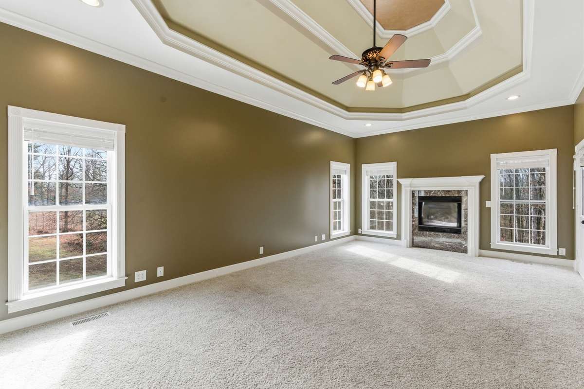 Spacious primary suite with a dramatic double-tray ceiling, cozy fireplace, and wall of windows that fill the room with natural light and peaceful views, creating a serene retreat to begin and end each day.