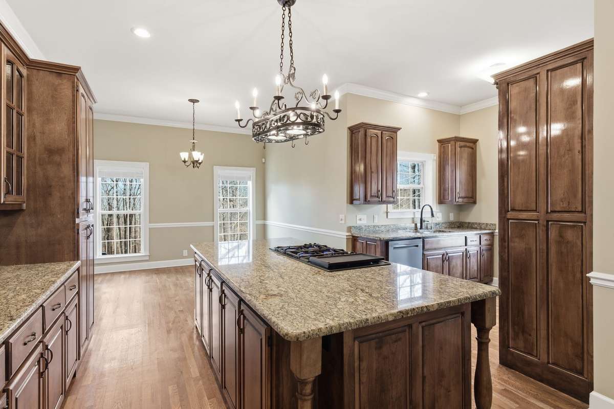 Upscale kitchen showcasing a large granite-topped island with Jenn‑Air cooktop, rich custom cabinetry, built‑in wine storage, and generous counter space, all opening to a cozy breakfast nook perfect for casual dining.