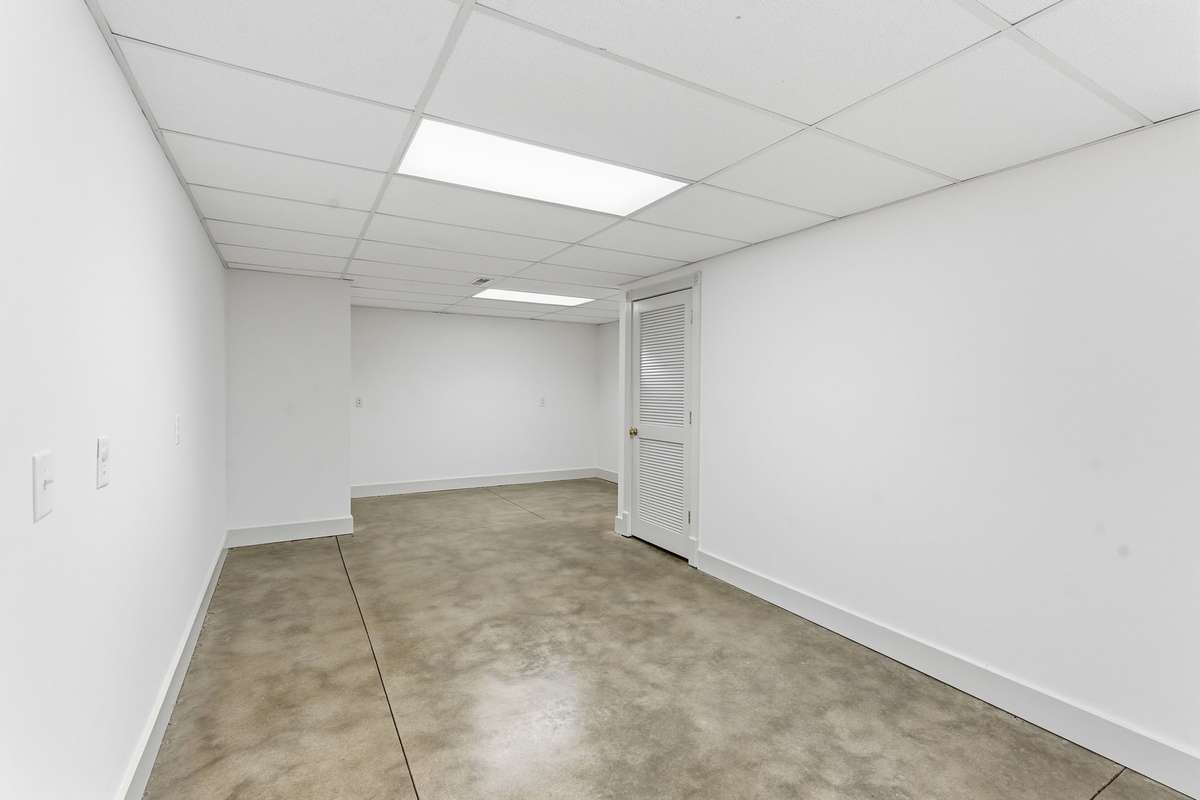 Expansive open area in the finished basement with polished concrete floors, neutral palette, and double doors to the backyard, offering a versatile space for a game room, gym, or large gatherings.