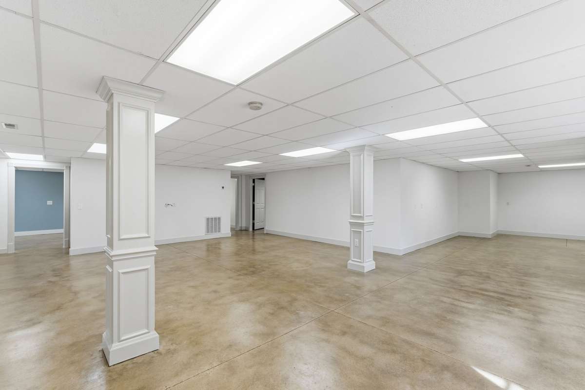 Expansive open area in the finished basement with polished concrete floors, neutral palette, and double doors to the backyard, offering a versatile space for a game room, gym, or large gatherings.