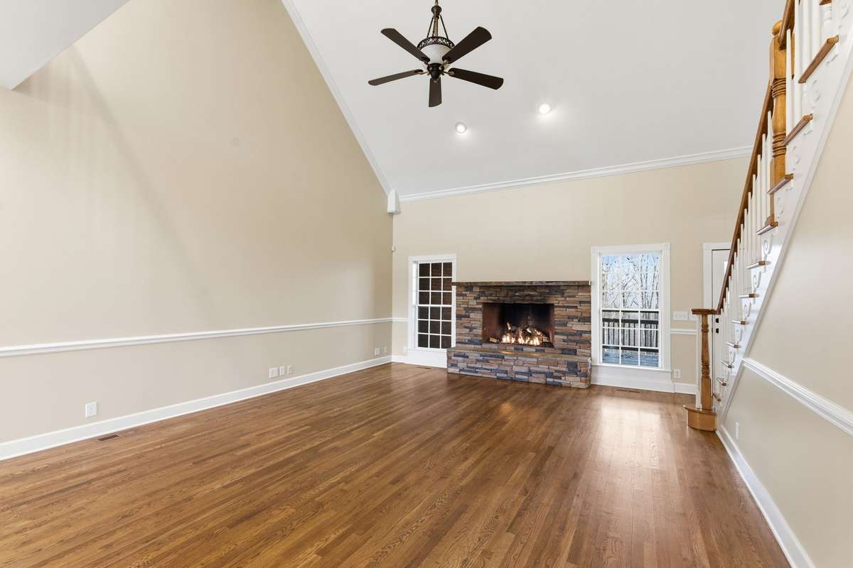 Main floor family/living room features a stacked-stone fireplace, soaring vaulted ceilings, and hardwood floors, with easy walkout access to the covered deck that is perfect for grilling, relaxing, and entertaining.