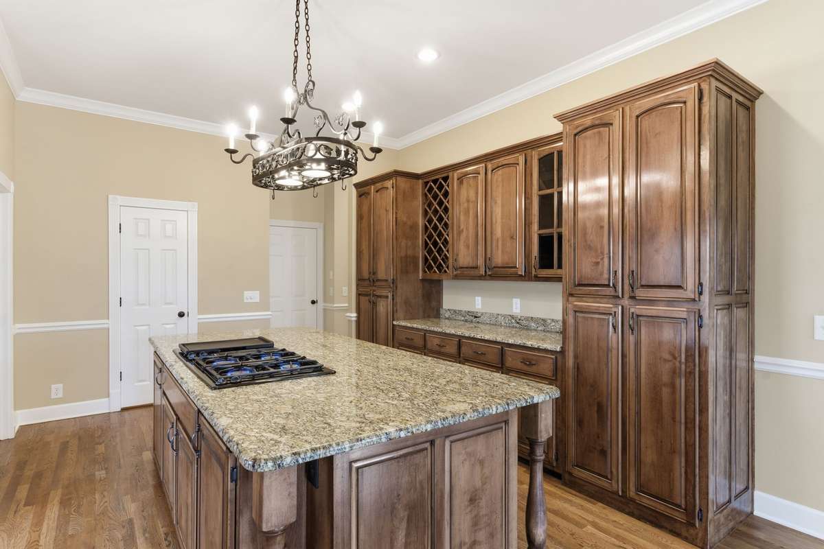 Upscale kitchen showcasing a large granite-topped island with Jenn‑Air cooktop, rich custom cabinetry, built‑in wine storage, and generous counter space, all opening to a cozy breakfast nook perfect for casual dining.