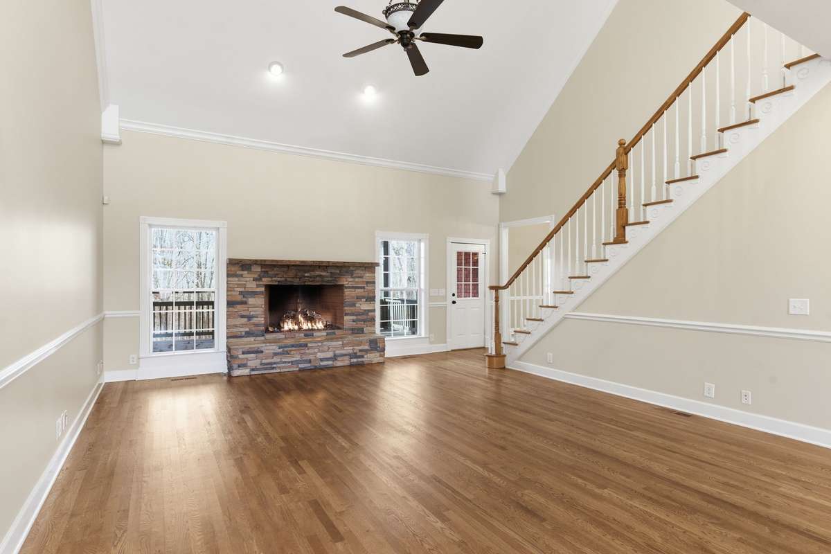 Main floor family/living room features a stacked-stone fireplace, soaring vaulted ceilings, and hardwood floors, with easy walkout access to the covered deck that is perfect for grilling, relaxing, and entertaining.