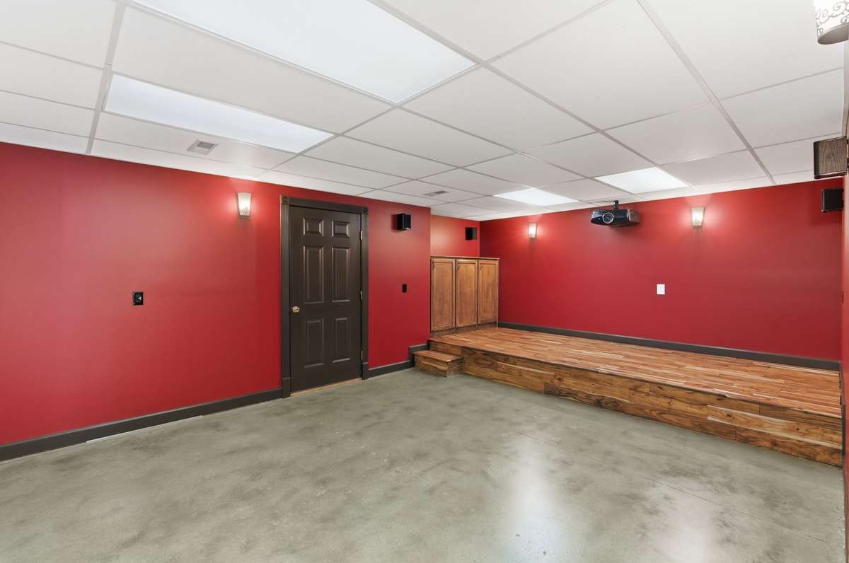 Downstairs theater room with bold cinema-style walls, built-in screen and speakers, and tiered flooring, creating the perfect space for movie nights, game days, and immersive entertainment at home.