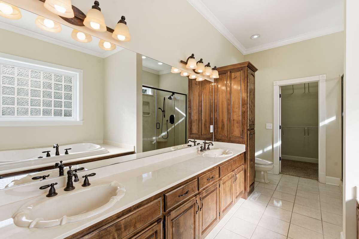 Luxurious primary bath featuring an extended double vanity with rich wood cabinetry, relaxing soaking tub, and large walk-in shower, all leading to an expansive walk-in closet for effortless organization.