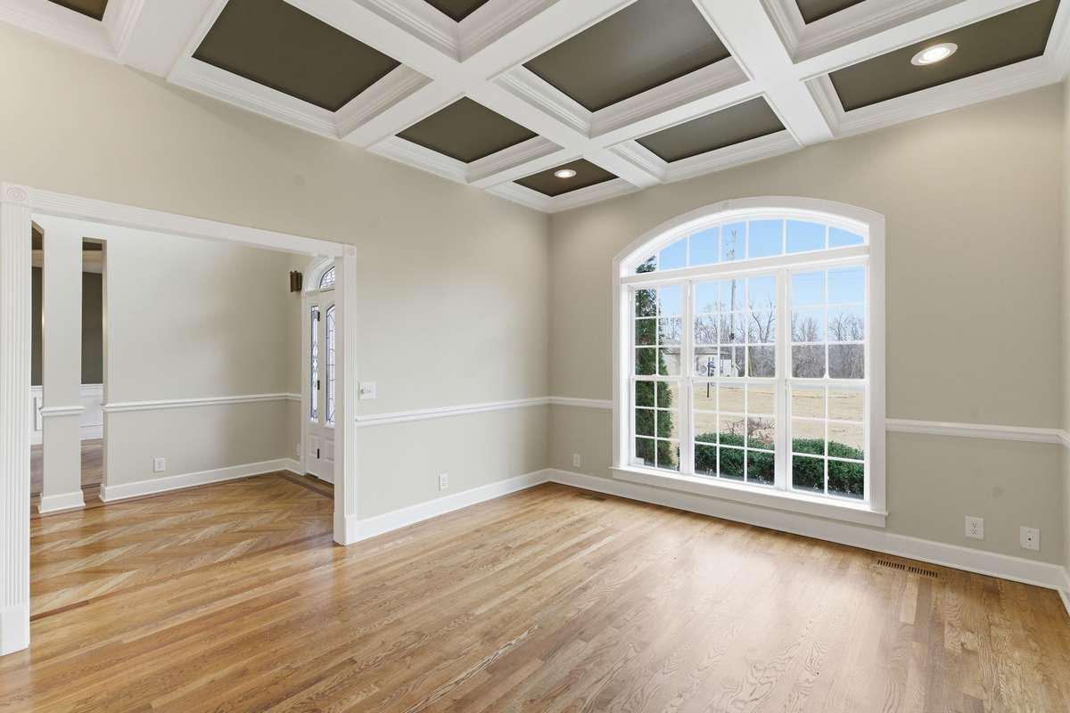 Sophisticated formal office or sitting room featuring rich hardwood floors, classic chair rail molding, and a dramatic coffered ceiling with recessed lighting, offering an elegant space for work, reading, or quiet conversation.