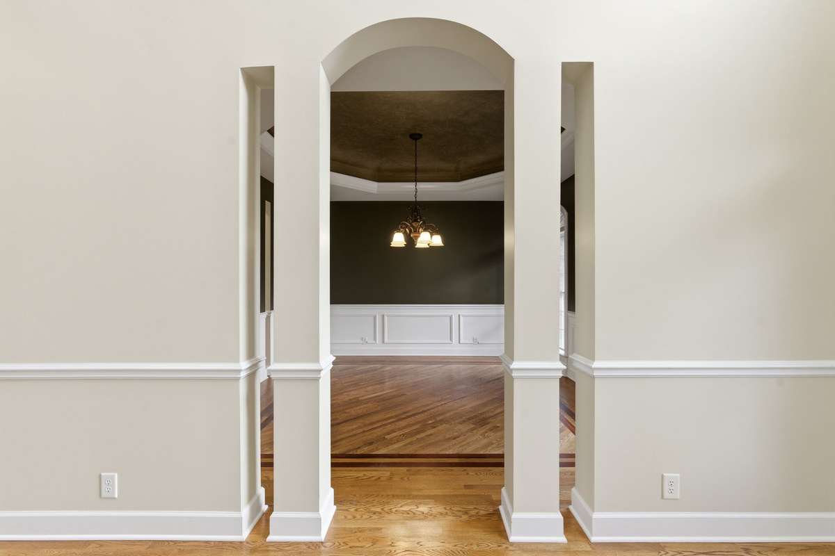 Elegant arched entry leading into the luxurious formal dining room, featuring custom painted tray ceiling, detailed wainscoting, and freshly professionally painted interiors throughout the home.