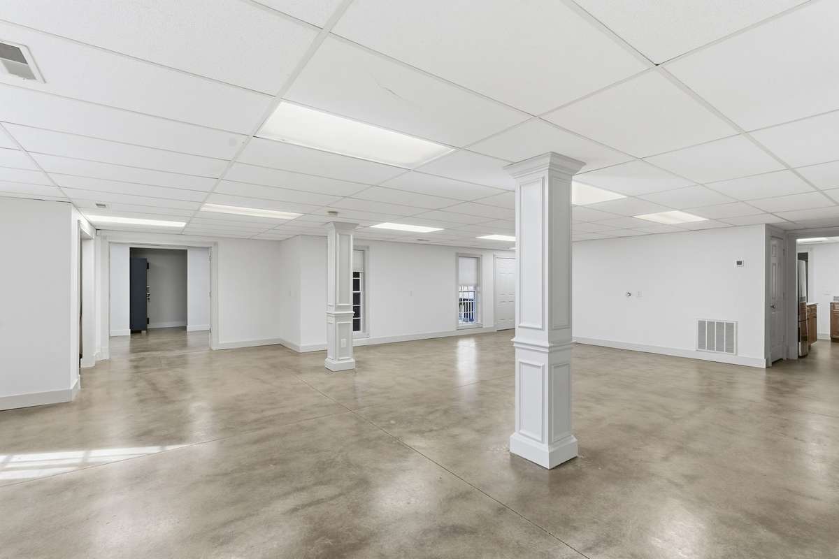Expansive open area in the finished basement with polished concrete floors, neutral palette, and double doors to the backyard, offering a versatile space for a game room, gym, or large gatherings.