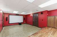 Downstairs theater room with bold cinema-style walls, built-in screen and speakers, and tiered flooring, creating the perfect space for movie nights, game days, and immersive entertainment at home.