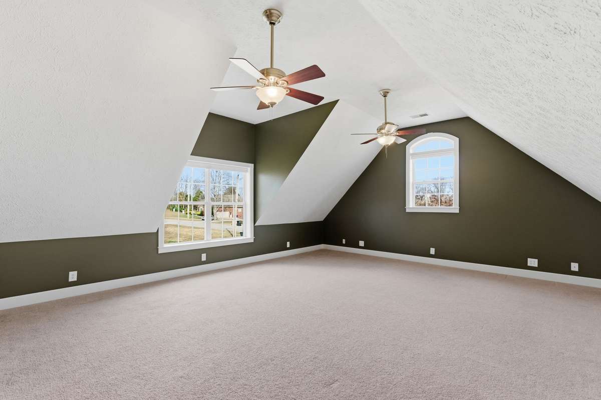 Expansive bonus room over the garage with unique architectural angles, dual ceiling fans, and large windows that bring in plenty of natural light—perfect for a media room, playroom, home gym, or additional living space.