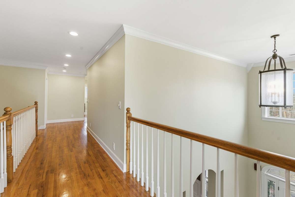 Upstairs hallway and catwalk with gleaming hardwood floors and open railing, offering a bright, airy overlook to the foyer below and easy access to the upper-level bedrooms and living spaces.