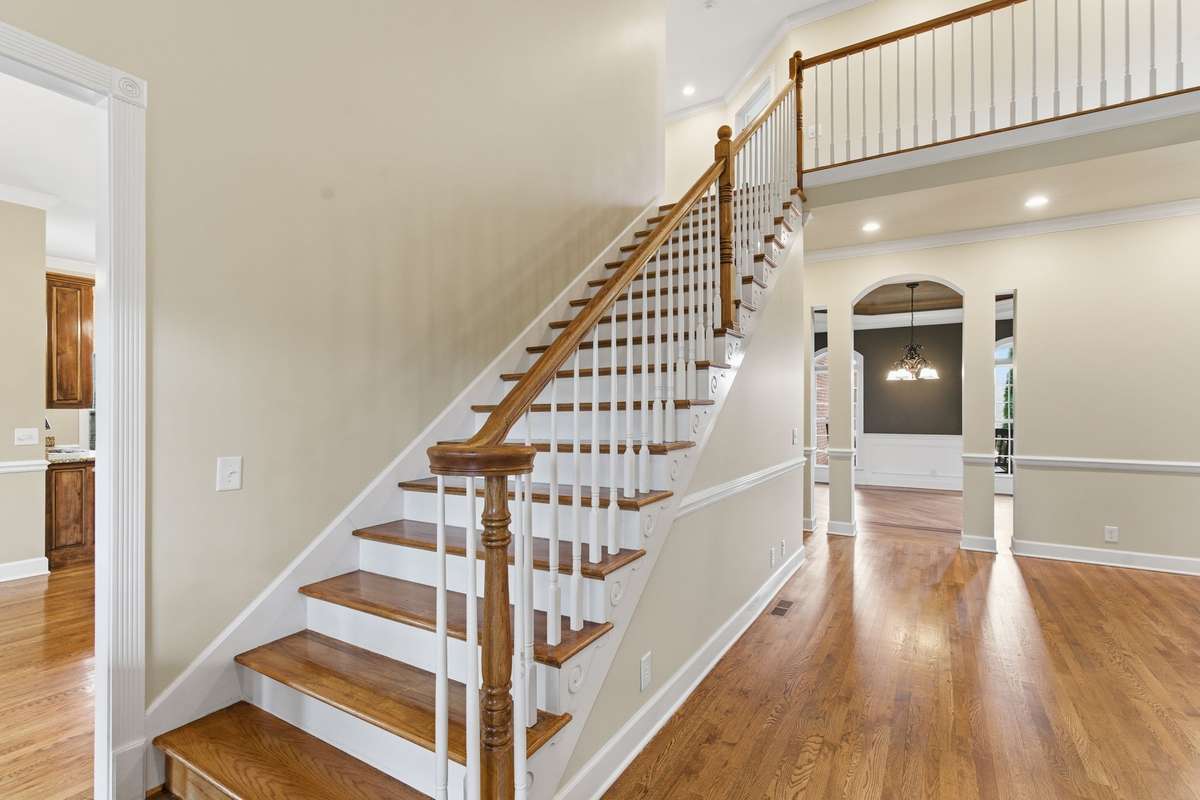 Grand staircase with hardwood treads and elegant wood-and-iron railing, welcoming you into the home and leading to the upper living areas with a beautiful open view of the main level.