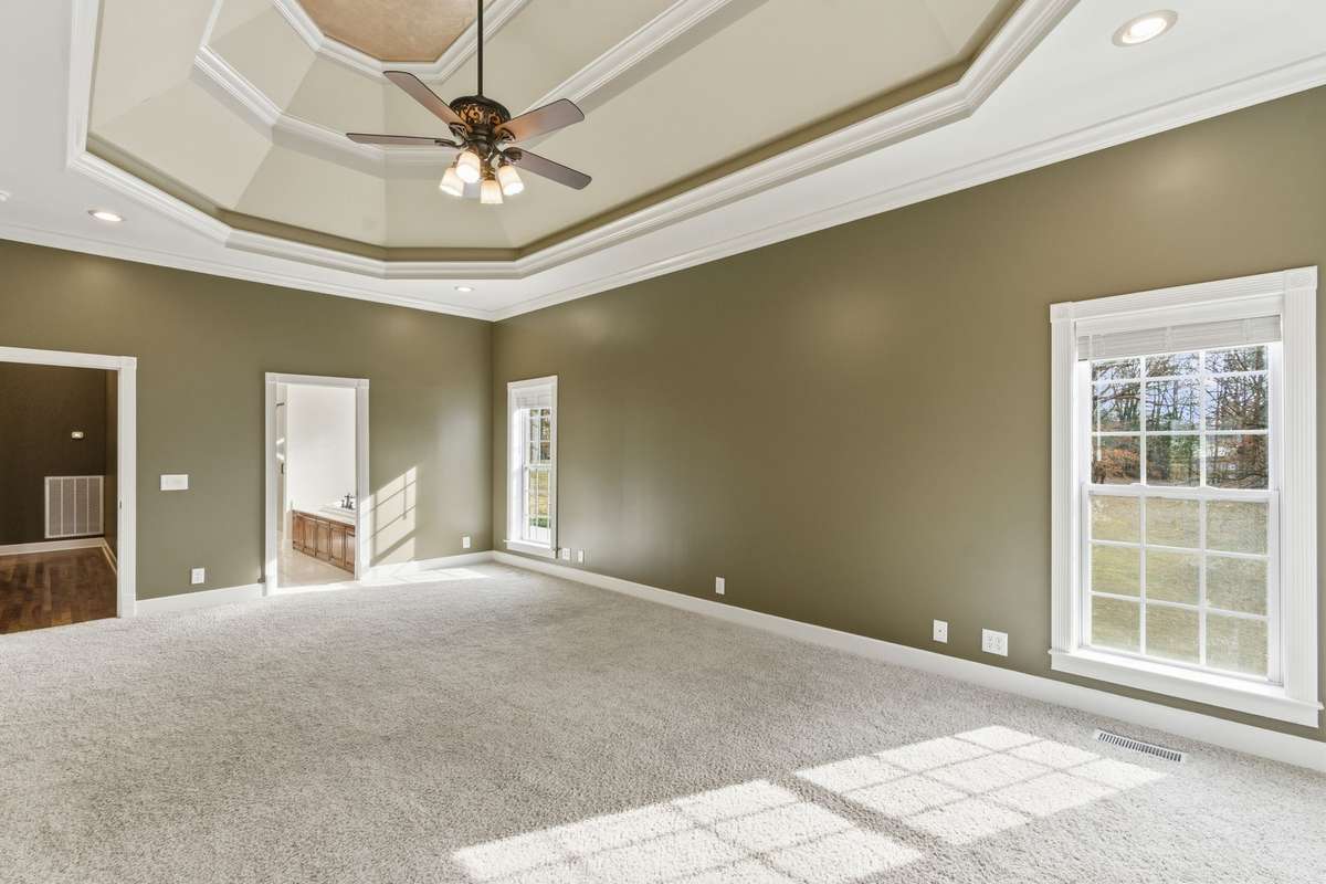 Spacious primary suite with a dramatic double-tray ceiling, cozy fireplace, and wall of windows that fill the room with natural light and peaceful views, creating a serene retreat to begin and end each day.