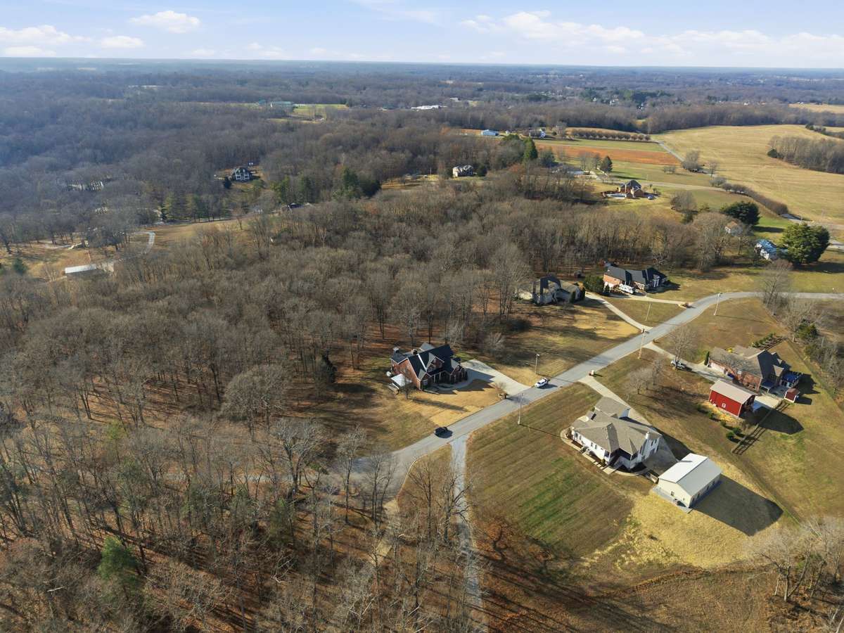 Aerial view of this stately all-brick home nestled on 4.01 acres, surrounded by mature trees for privacy and peaceful country-style living just minutes from town.
