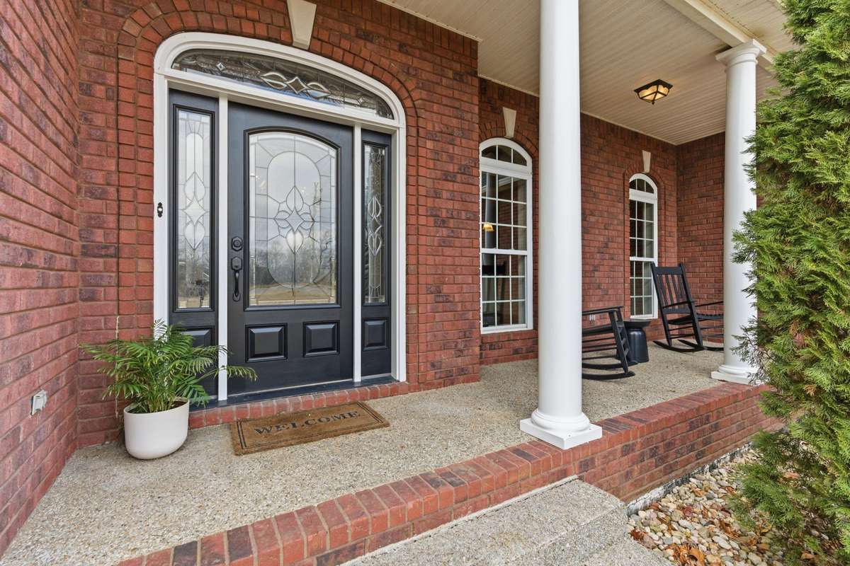 Charming covered front porch with classic columns, decorative glass double doors, and room for rocking chairs, creating a warm Southern welcome the moment you arrive.
