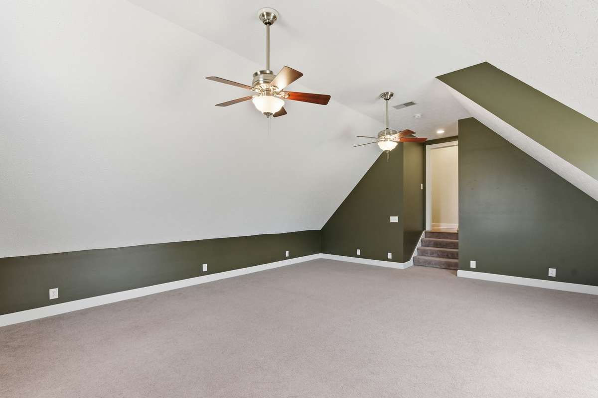 Expansive bonus room over the garage with unique architectural angles, dual ceiling fans, and large windows that bring in plenty of natural light—perfect for a media room, playroom, home gym, or additional living space.