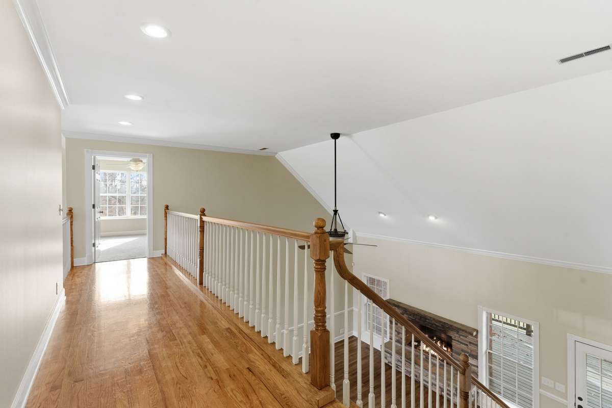 Upstairs hallway and catwalk with gleaming hardwood floors and open railing, offering a bright, airy overlook to the foyer below and easy access to the upper-level bedrooms and living spaces.