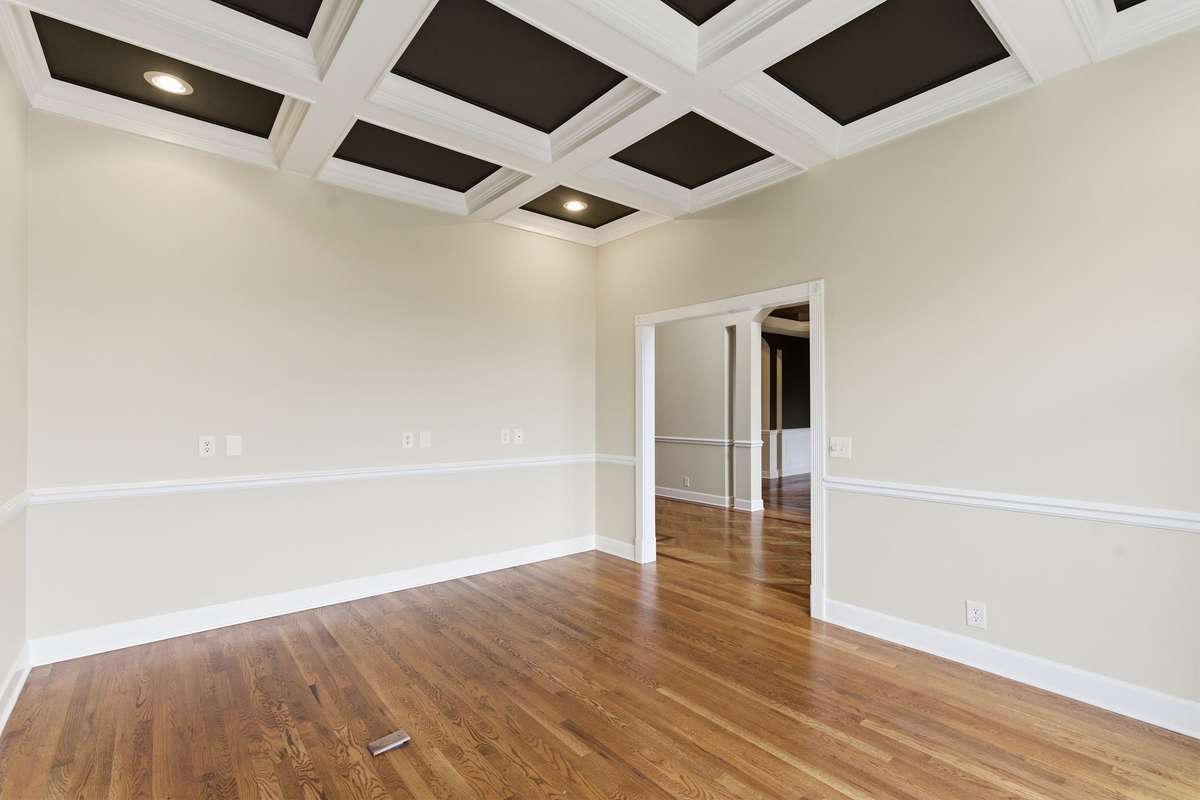 Sophisticated formal office or sitting room featuring rich hardwood floors, classic chair rail molding, and a dramatic coffered ceiling with recessed lighting, offering an elegant space for work, reading, or quiet conversation.