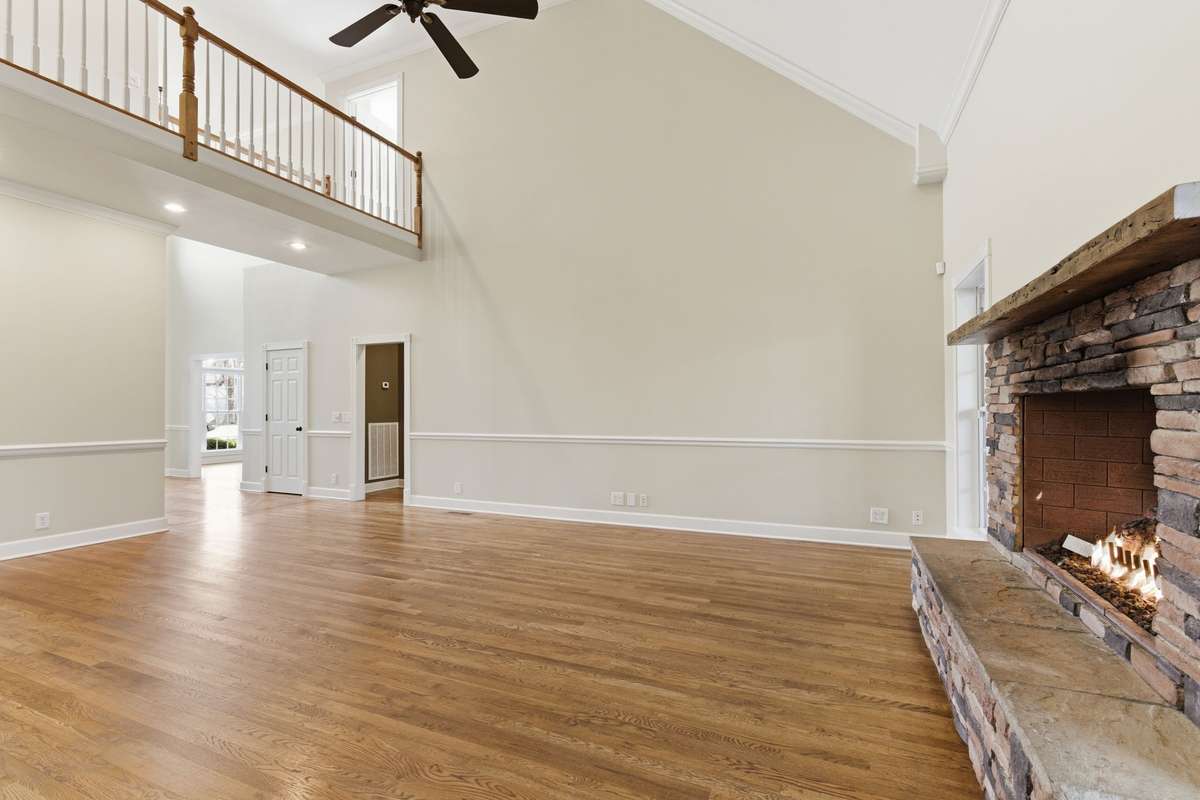 Main floor family/living room features a stacked-stone fireplace, soaring vaulted ceilings, and hardwood floors, with easy walkout access to the covered deck that is perfect for grilling, relaxing, and entertaining.
