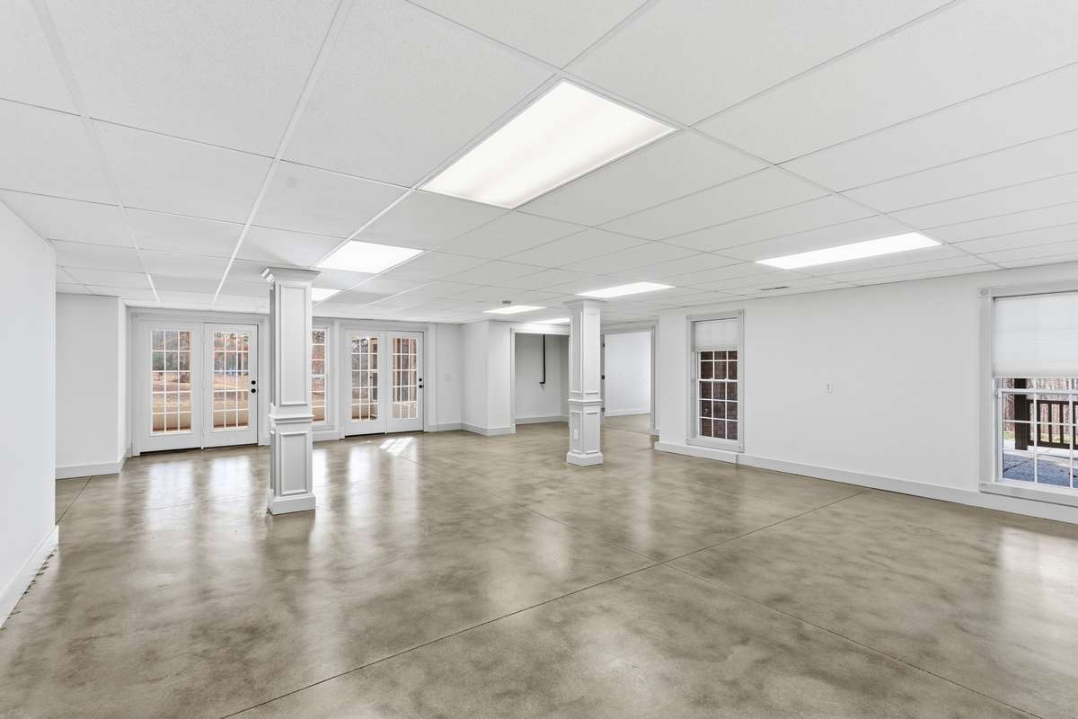 Expansive open area in the finished basement with polished concrete floors, neutral palette, and double doors to the backyard, offering a versatile space for a game room, gym, or large gatherings.