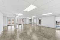 Expansive open area in the finished basement with polished concrete floors, neutral palette, and double doors to the backyard, offering a versatile space for a game room, gym, or large gatherings.