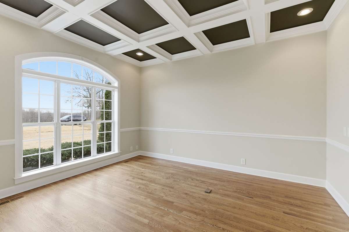 Sophisticated formal office or sitting room featuring rich hardwood floors, classic chair rail molding, and a dramatic coffered ceiling with recessed lighting, offering an elegant space for work, reading, or quiet conversation.
