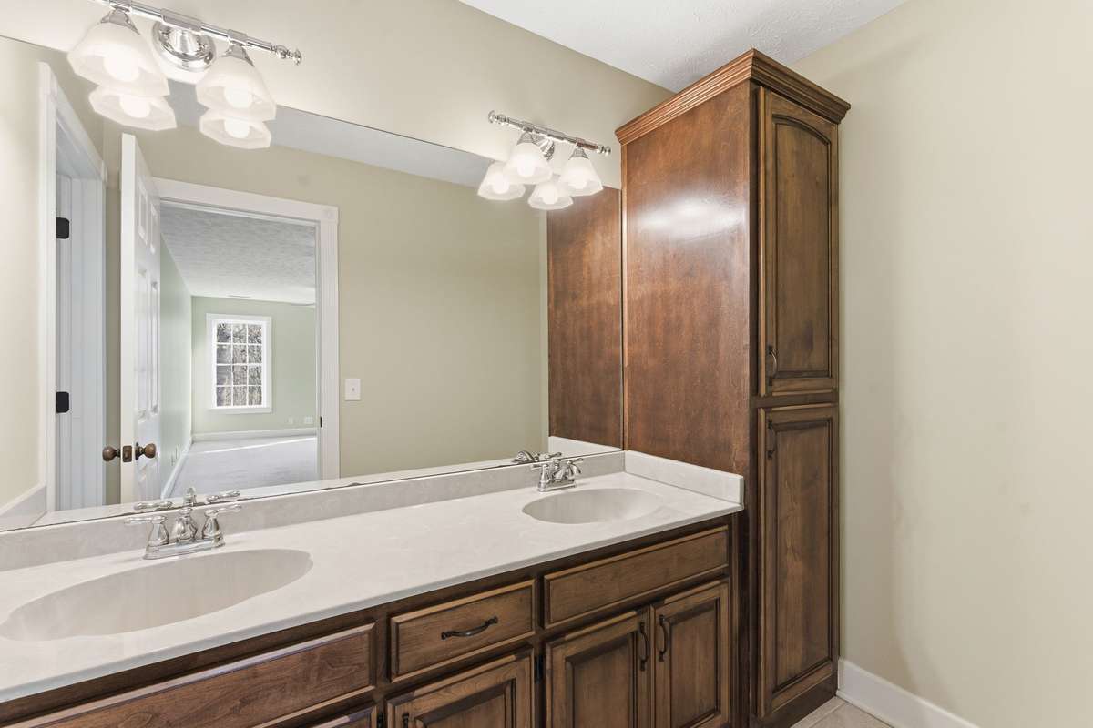 Spacious upstairs secondary primary bedroom featuring two ceiling fans, soft natural light from double windows, a private en-suite bath, and an oversized walk-in closet for exceptional storage.