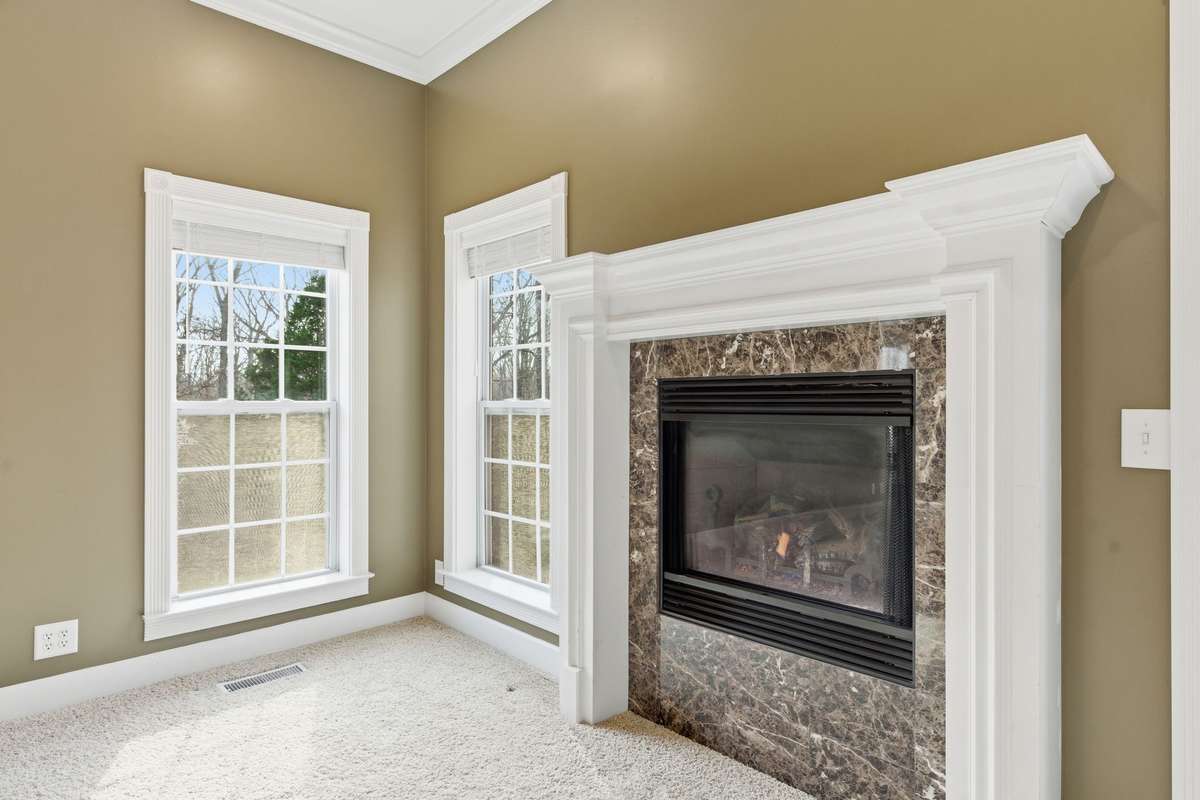 Spacious primary suite with a dramatic double-tray ceiling, cozy fireplace, and wall of windows that fill the room with natural light and peaceful views, creating a serene retreat to begin and end each day.