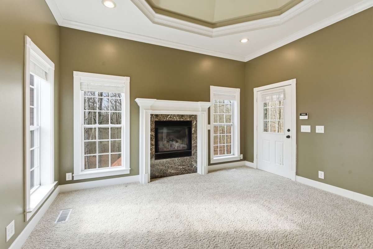 Spacious primary suite with a dramatic double-tray ceiling, cozy fireplace, and wall of windows that fill the room with natural light and peaceful views, creating a serene retreat to begin and end each day.
