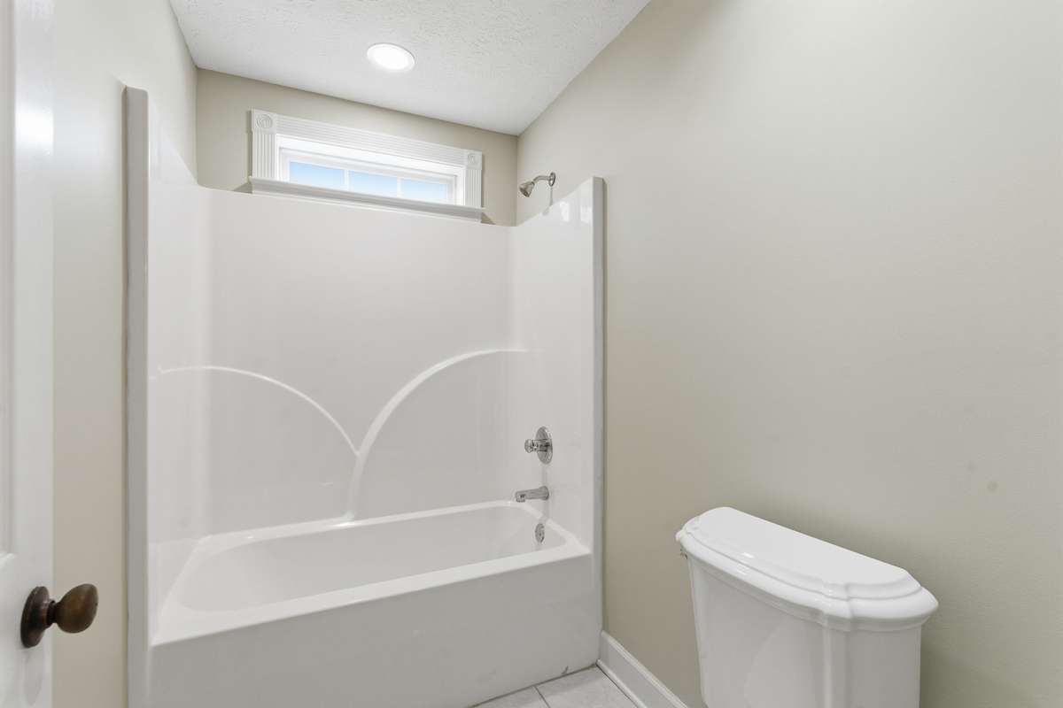 Spacious upstairs secondary primary bedroom featuring two ceiling fans, soft natural light from double windows, a private en-suite bath, and an oversized walk-in closet for exceptional storage.