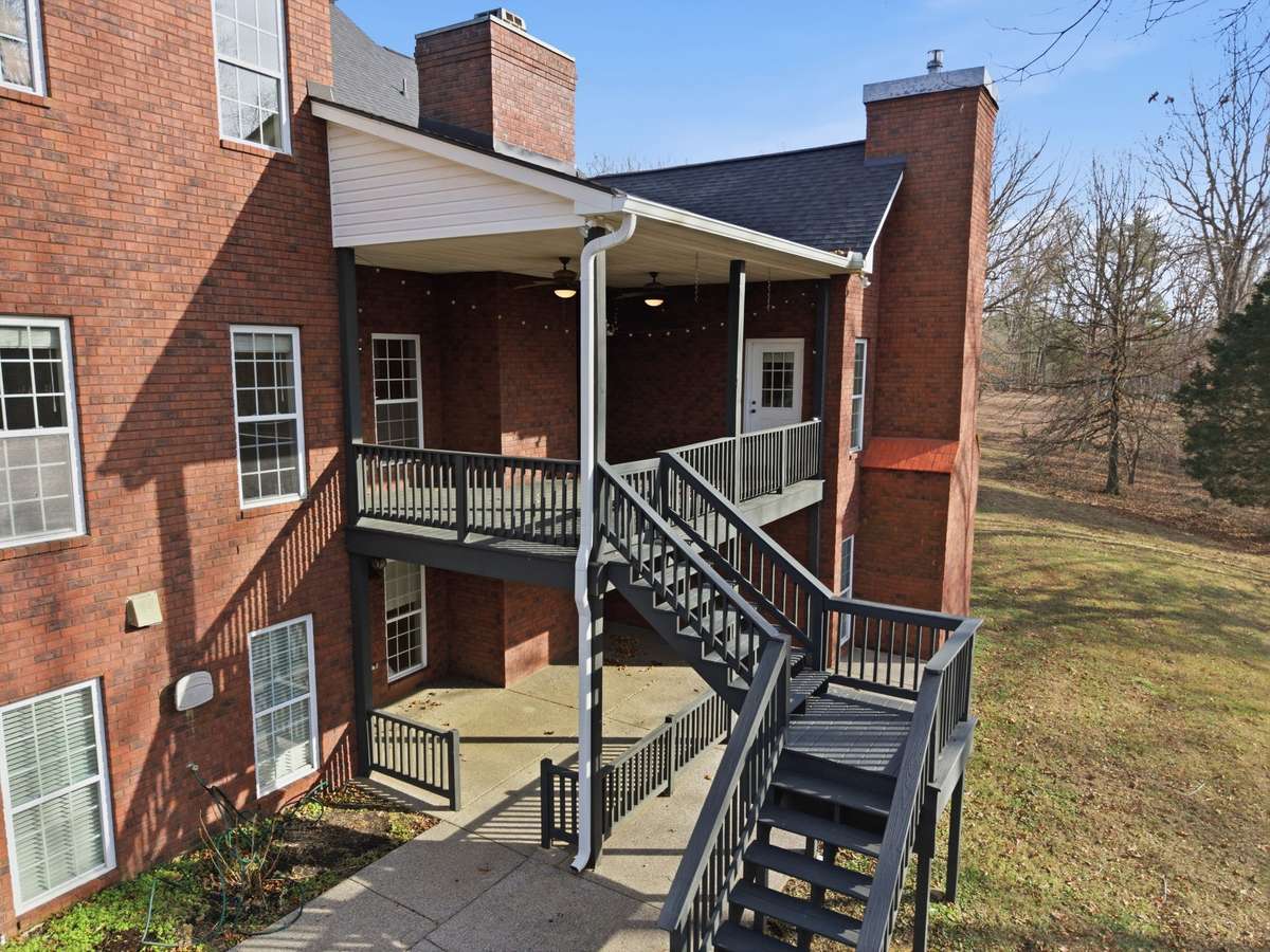 All-brick estate exterior showcasing classic architecture, upper and lower covered patios, and a custom staircase leading to the walkout basement, all set on a spacious corner lot in Portland’s prestigious Dogwood Springs neighborhood.