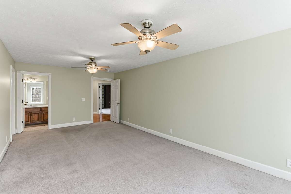 Spacious upstairs secondary primary bedroom featuring two ceiling fans, soft natural light from double windows, a private en-suite bath, and an oversized walk-in closet for exceptional storage.