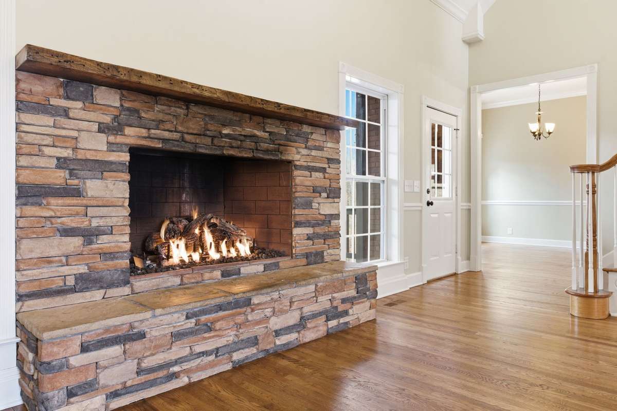Main floor family/living room features a stacked-stone fireplace, soaring vaulted ceilings, and hardwood floors, with easy walkout access to the covered deck that is perfect for grilling, relaxing, and entertaining.