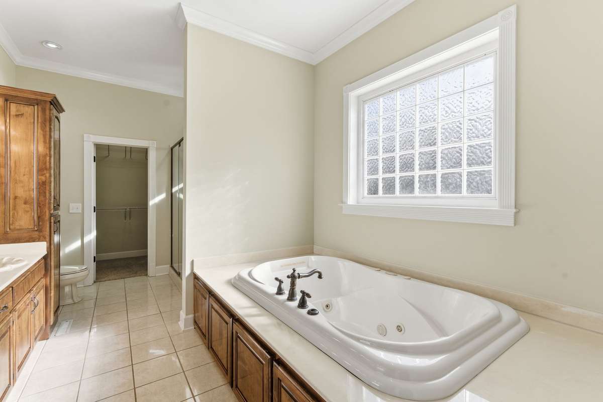 Luxurious primary bath featuring an extended double vanity with rich wood cabinetry, relaxing soaking tub, and large walk-in shower, all leading to an expansive walk-in closet for effortless organization.