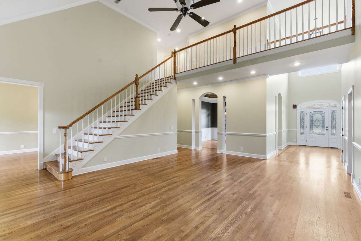Impressive two-story family/living room featuring rich hardwood floors, a sweeping staircase with overlook, and an open layout that flows beautifully for everyday living and entertaining.