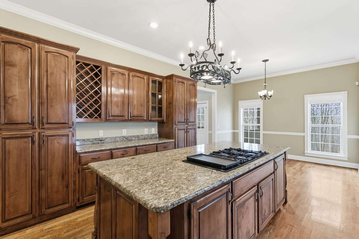 Upscale kitchen showcasing a large granite-topped island with Jenn‑Air cooktop, rich custom cabinetry, built‑in wine storage, and generous counter space, all opening to a cozy breakfast nook perfect for casual dining.