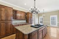 Upscale kitchen showcasing a large granite-topped island with Jenn‑Air cooktop, rich custom cabinetry, built‑in wine storage, and generous counter space, all opening to a cozy breakfast nook perfect for casual dining.