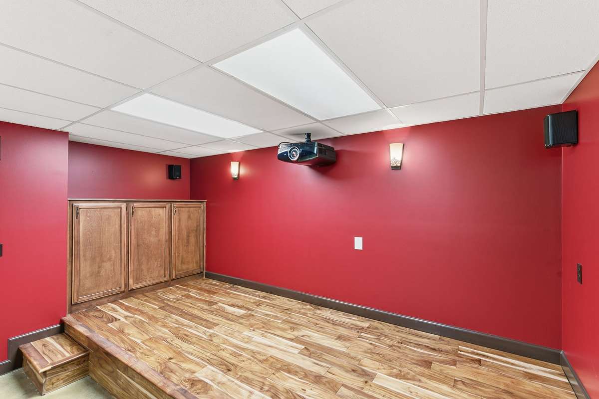 Downstairs theater room with bold cinema-style walls, built-in screen and speakers, and tiered flooring, creating the perfect space for movie nights, game days, and immersive entertainment at home.