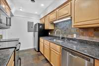 Galley-style kitchen featuring granite countertops, slate backsplash, and stainless appliances.